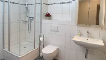 Ein modernes Badezimmer mit einer Duschkabine, einer weißen Toilette und einem Waschbecken mit Spiegel darüber.