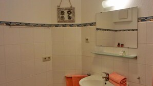 Ein Badezimmer mit weiß gefliesten Wänden, einem weißen Waschbecken, einem Spiegel und einem Handtuchhalter.
