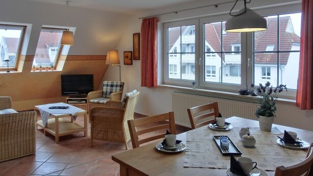 Ein gemütliches Wohnzimmer mit Fernseher, Korbmöbeln und einem Essbereich mit Tisch für vier Personen.