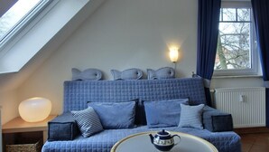 A cozy room with a blue sofa, a small table with a teapot, and a window with curtains. - Apartment H 07 - Apartment near the beach for 4 + 1 people, with WLAN (Graal-Müritz)