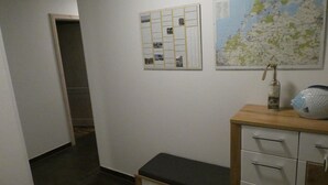 Ein Flur mit einer hölzernen Bank, einem Schrank mit Schubladen, einer Karte an der Wand und einer gerahmten Fotocollage.