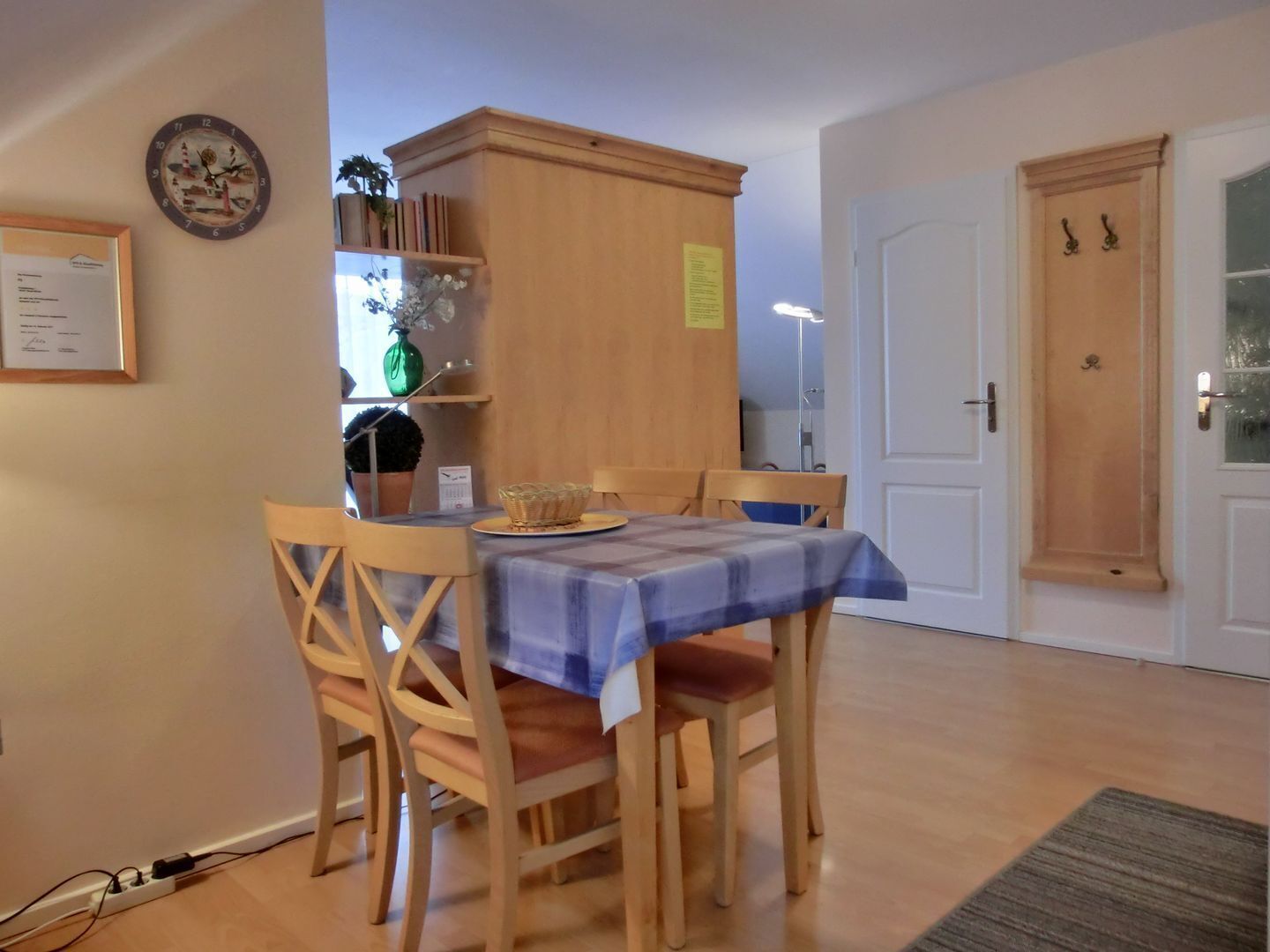 Ein Essbereich mit einem Tisch, der mit einer blauen Tischdecke bedeckt ist, Holzsesseln, einer Schrank mit Regalen und einer Tür mit Fensterteil.