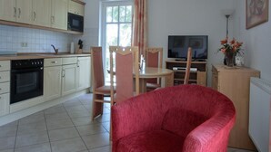 A compact kitchen with a microwave, stove, and cabinets. There is a dining area with a TV, a red chair, and a vase with flowers. - Apartment T7 - 2-room apartment for 4 pers. on the upper floor. Close to the beach (Graal-Müritz)