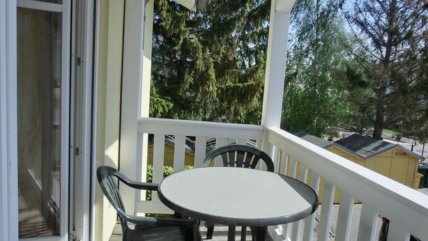 A covered outdoor area with a round table and four chairs, a white railing, and a view of trees and a building in the background. - Apartment T7 - 2-room apartment for 4 pers. on the upper floor. Close to the beach (Graal-Müritz)