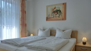 A double bed with white linens, two bedside tables with lamps, a painting on the wall, and a window with sheer curtains. - Apartment T7 - 2-room apartment for 4 pers. on the upper floor. Close to the beach (Graal-Müritz)