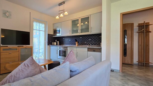 A modern kitchen with a flat-screen TV, wooden cabinets, and a dining area with a table and cushions.