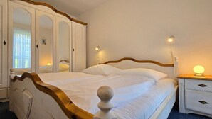 A bedroom with a large bed, a wardrobe, a bedside table with a lamp, and a window with curtains.