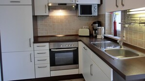 Una cocina compacta con armarios blancos, un microondas, un tostador, una tetera y un lavabo.