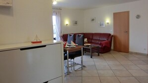 Un espacio habitable pequeño con kitchenette, un sofá de cuero rojo, una mesa de comedor con sillas y una ventana pequeña con cortinas.