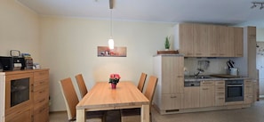Una cocina compacta con armarios de madera, una mesa de comedor con sillas y una lámpara colgante.