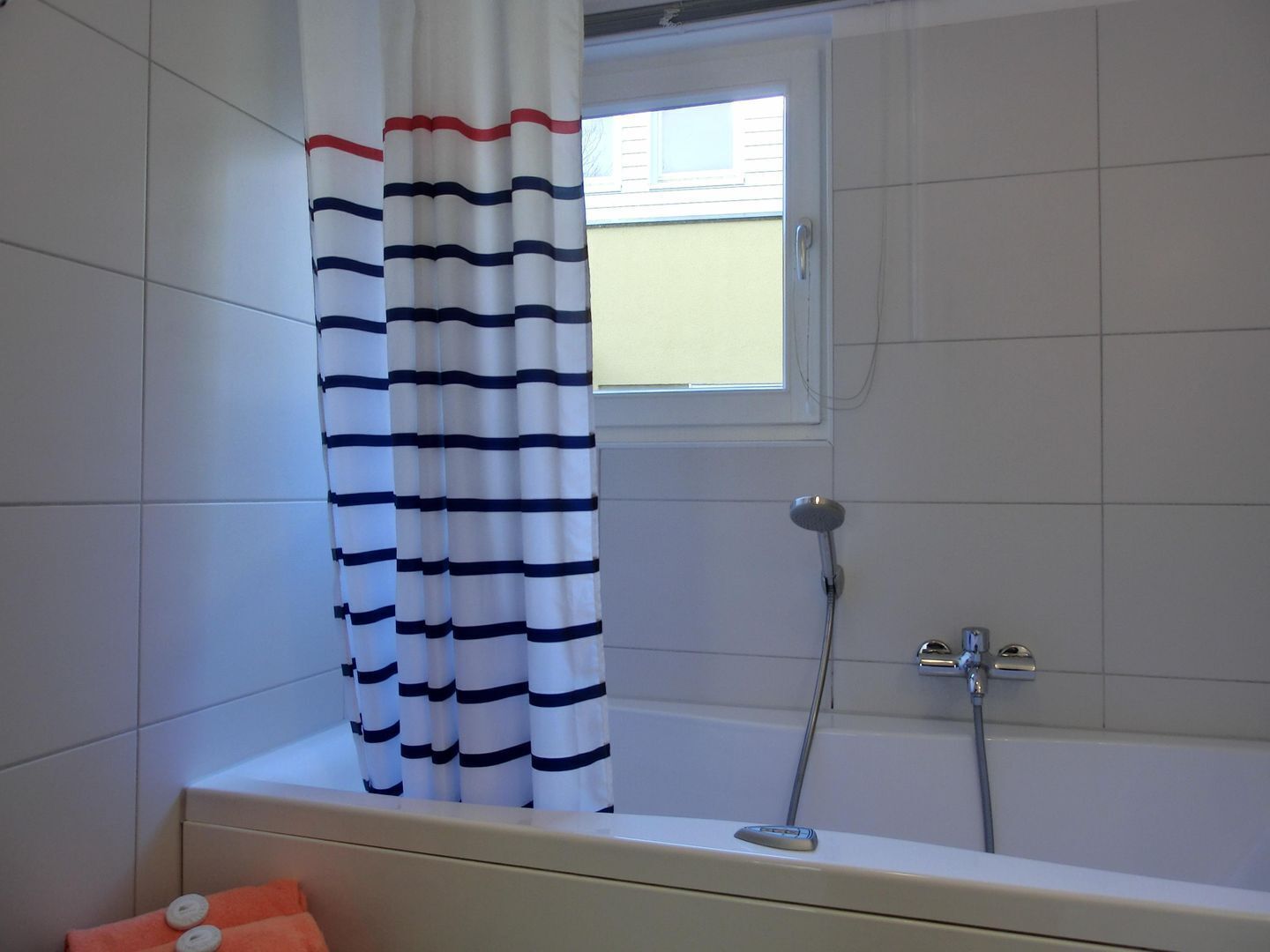 Une salle de bain avec une baignoire, une douche et une fenêtre donnant sur un immeuble.