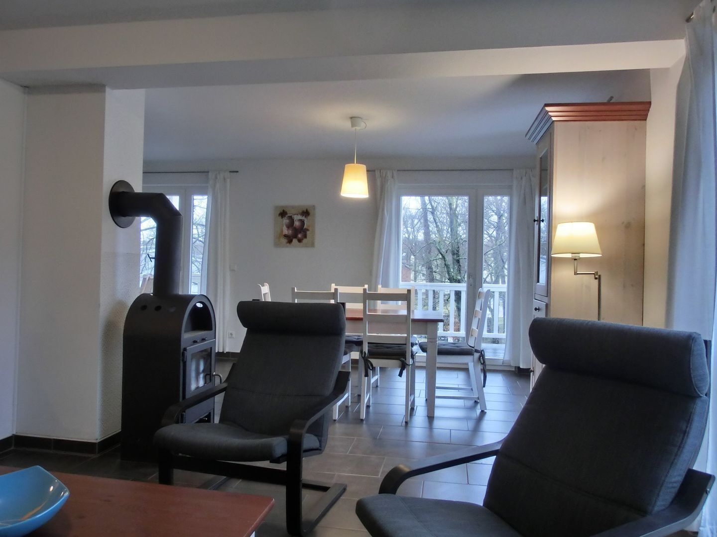 Een moderne woonkamer met een open haard, twee fauteuils, een eettafel en uitzicht op de omgeving door grote ramen.