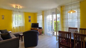 Una sala de estar con paredes amarillas, un sofá, una silla, un televisor sobre un mueble de madera y una mesa de comedor con sillas.