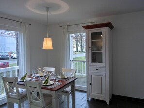 A dining area with a table set for four, white chairs, a wooden cabinet, and a hanging light fixture.