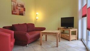 Een woonkamer met een rode bank, een houten salontafel, een televisie op een houten standaard en een schilderij aan de muur.