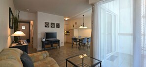 A living room with a sofa, a TV, a dining table with chairs, and a kitchen area in the background. - Apartment i26 - 2-room apartment near the beach on the 1st floor for 3 pers. (Graal-Müritz)