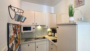 Une cuisine compacte avec des meubles blancs, un four à micro-ondes, une bouilloire et un petit évier.