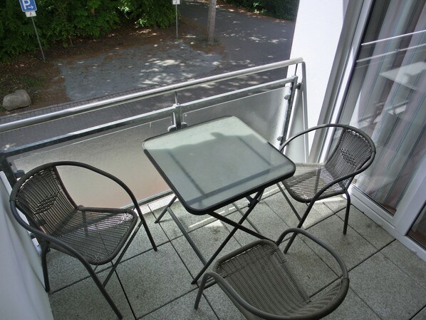Ein Balkon mit zwei Metallstühlen und einem kleinen Tisch, mit Blick auf einen Parkplatz und Grünflächen.