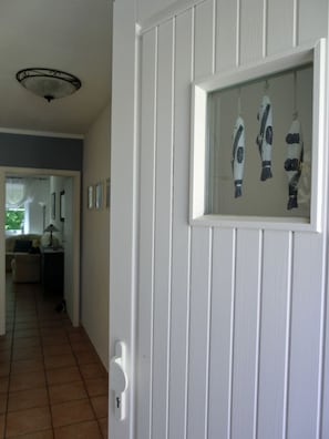 Eine weiße Tür mit Fenster, das Fische zeigt, ein gefliestes Podest und ein Flur, der in einen Wohnbereich führt.