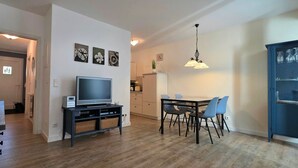 Un salon moderne doté d’un téléviseur à écran plat, d’une table à manger avec des chaises, d’un coin cuisine et d’un meuble bleu.