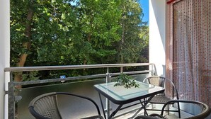 Un balcon avec une table et des chaises, un pot de fleurs et une vue sur les arbres.