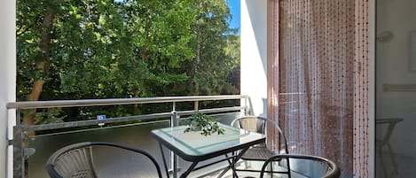 Un balcón con mesa y sillas, una planta en maceta y vistas a árboles.