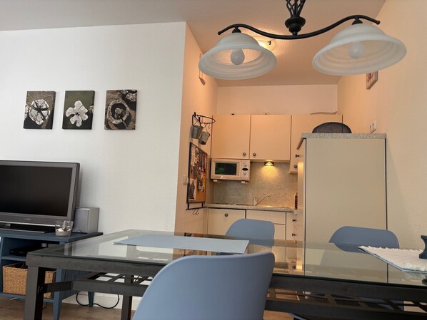 A modern kitchen with a microwave, refrigerator, and a dining area with a glass table and chairs.