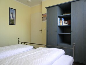 A room with two beds, a wardrobe, a framed picture on the wall, and a door.