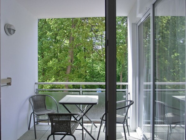 Ein Balkon mit Tisch und Stühlen, einer Glastür und Blick auf Bäume.