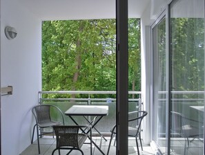 A balcony with a table and chairs, a glass door, and a view of trees.