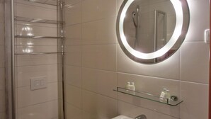 Un bagno con box doccia in vetro, uno specchio tondo illuminato e un lavabo con ripiano in vetro sopra.