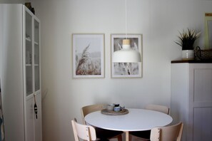 Un coin repas comprenant une table ronde, quatre chaises, deux tableaux encadrés, un luminaire suspendu et un buffet.