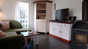 A living room with a green sofa, a white cabinet, a television, and a wood-burning stove.
