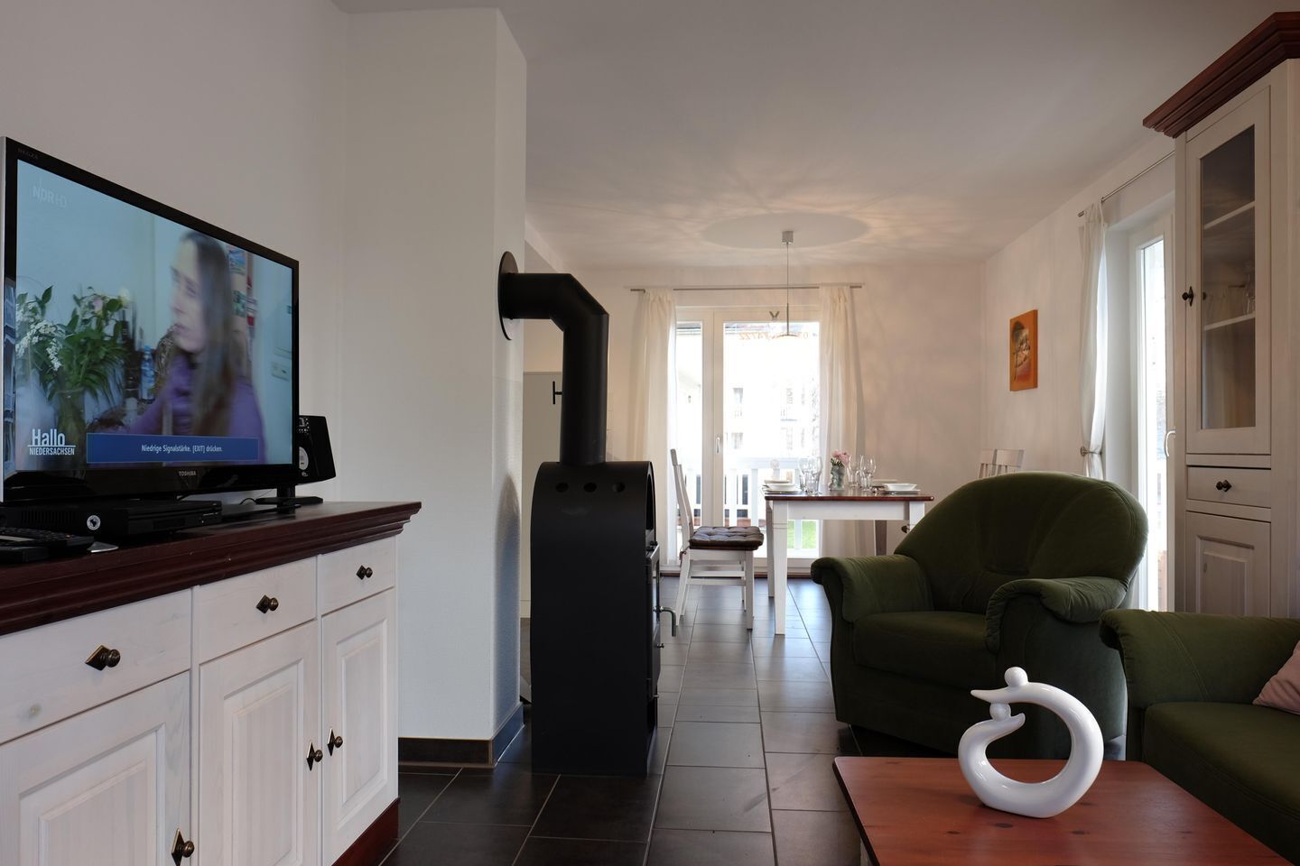 Una sala de estar con televisor, sofá, mesa y un objeto decorativo.