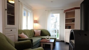 A cozy living room with a green sofa, a small table, a lamp, and a kitchen area with a stove.