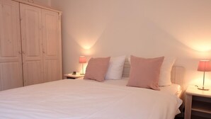 A bedroom with a large bed, two bedside tables with lamps, and a wardrobe.
