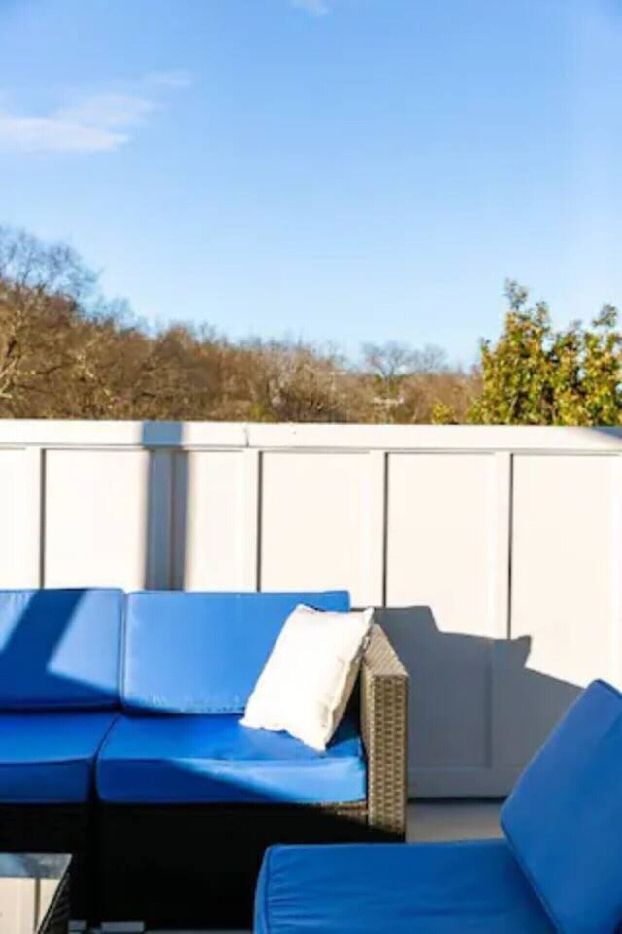 A blue outdoor seating area with a white cushion, a wicker chair, and a white wall in the background.