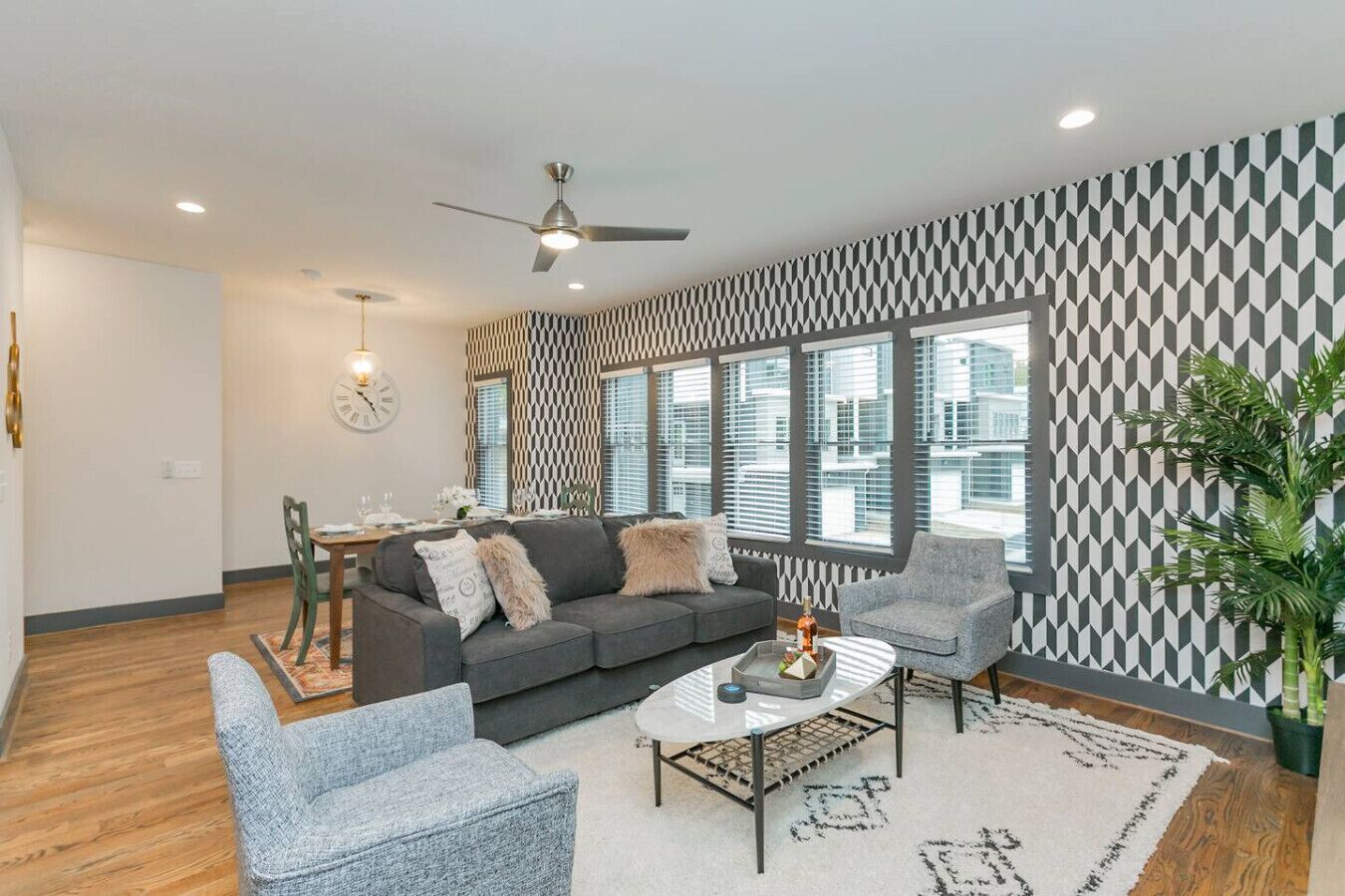 Un salon moderne avec un canapé gris, deux fauteuils, une table basse et un coin repas comprenant une table et des chaises.