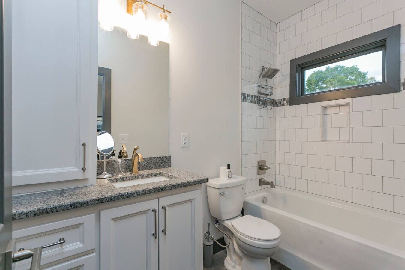 Une salle de bain moderne avec un comptoir en granit, des toilettes, une baignoire et une fenêtre située au-dessus de la baignoire.