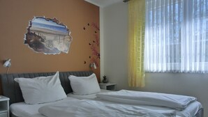 A double bed with white linens, a grey headboard, and a wall-mounted lamp.