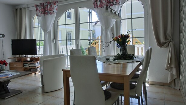 A dining area with a table, chairs, a TV, and a window with curtains.