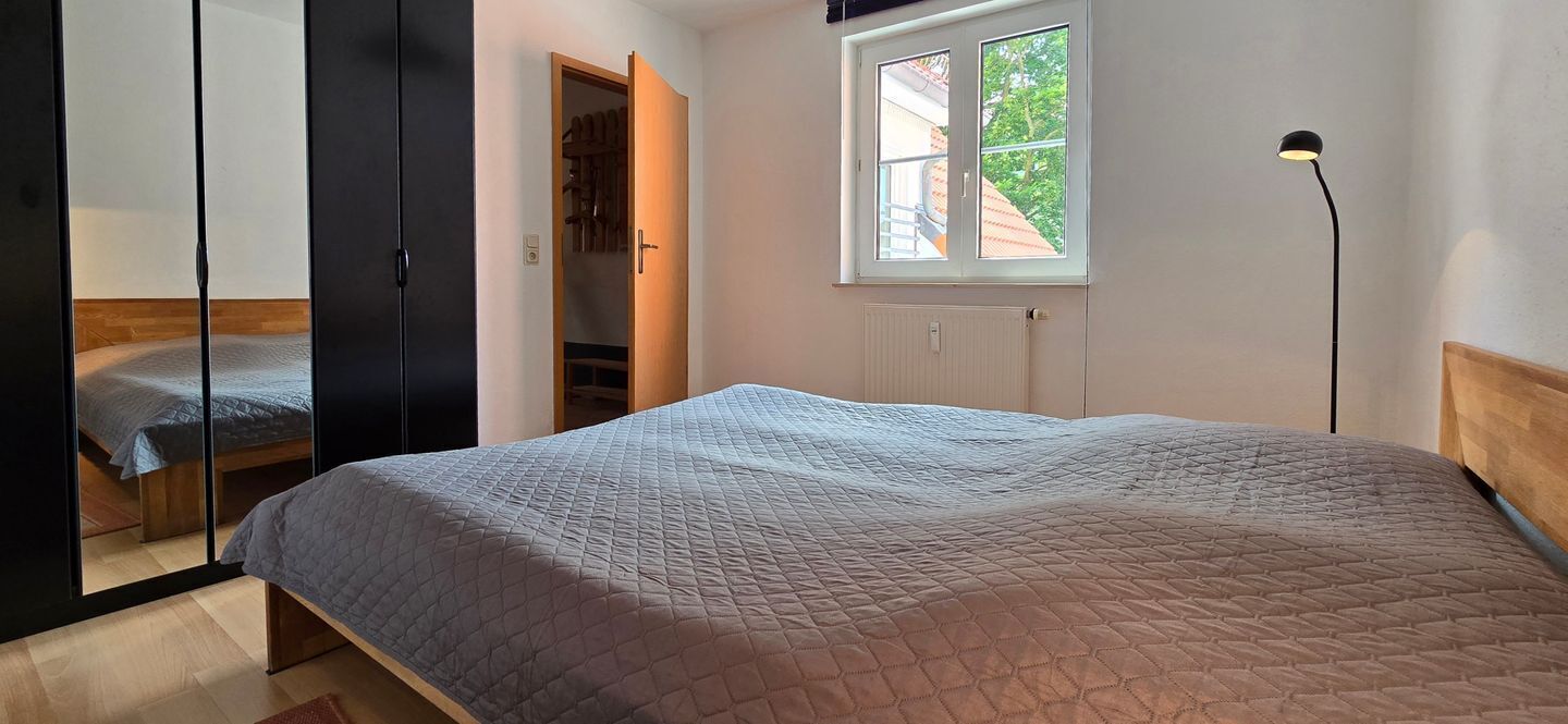 A bedroom with a bed, a wardrobe, a window, and a floor lamp.