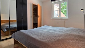 Un dormitorio con cama, armario, ventana y lámpara de pie.