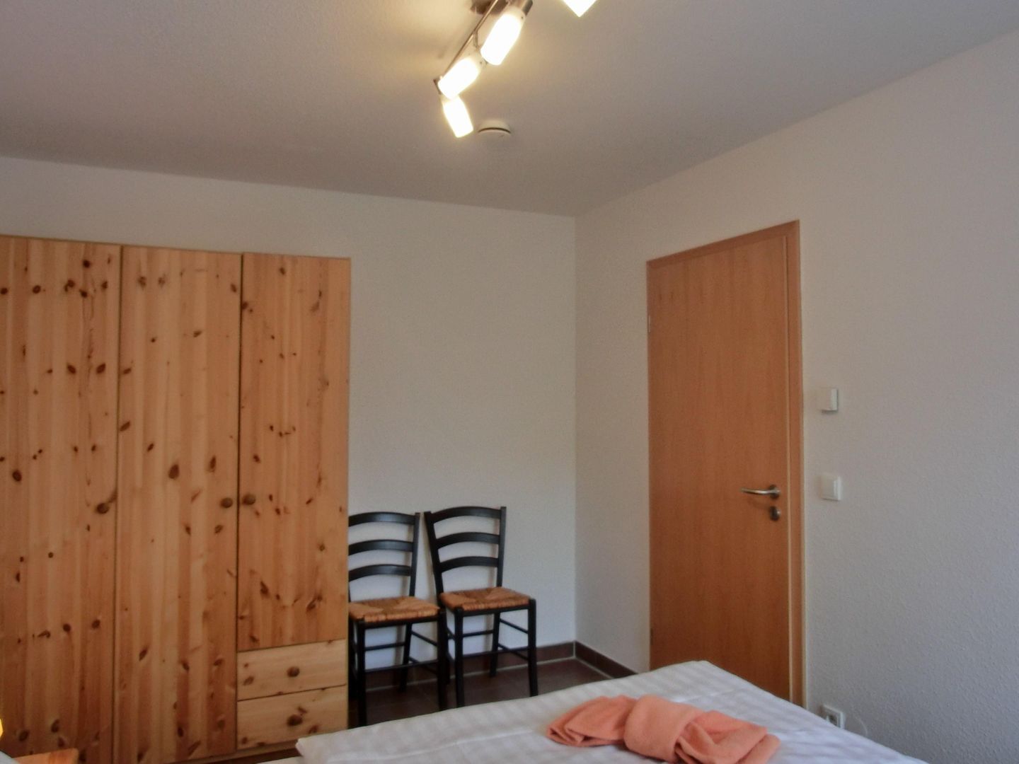 Une chambre à coucher avec un lit, une armoire en bois, deux chaises et une porte.