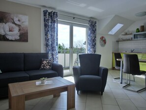 Un salon avec un canapé, une table basse et un fauteuil. Il y a un balcon qui offre une vue sur l’extérieur.