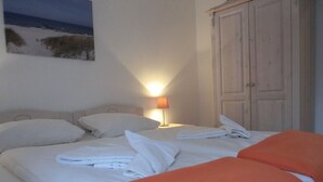Ein Hotelzimmer mit einem Bett, einem Nachttisch mit Lampe, einem Kleiderschrank und einem Bild mit Strandmotiv.