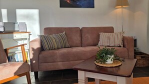 Ein Wohnzimmer mit braunem Sofa, gestreifter Dekokissen, einem kleinen Tisch mit Pflanze, einer Lampe und einem Kaminofen.