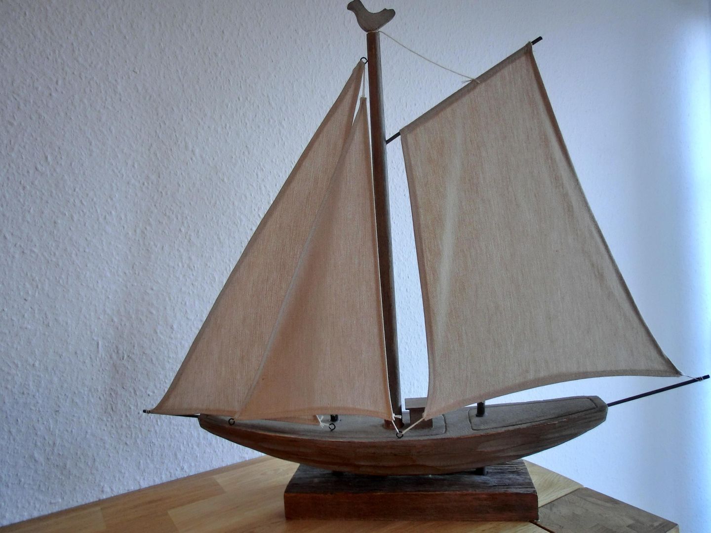 A wooden model sailboat on a wooden base.