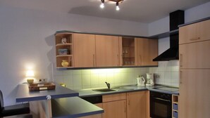 A compact kitchen with wooden cabinets, a sink, a stove, and a coffee maker. - Apartment O2 - 2-room apartment for 3 pers. on the ground floor with south-west facing terrace (Graal-Müritz)
