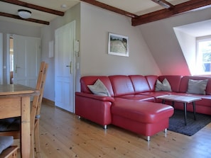 Een rode leren bank, een houten eettafel en stoelen in een kamer met houten vloeren en een schuine plafond.